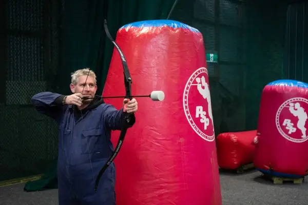 Archery tag player drawing a bow behind a bunker